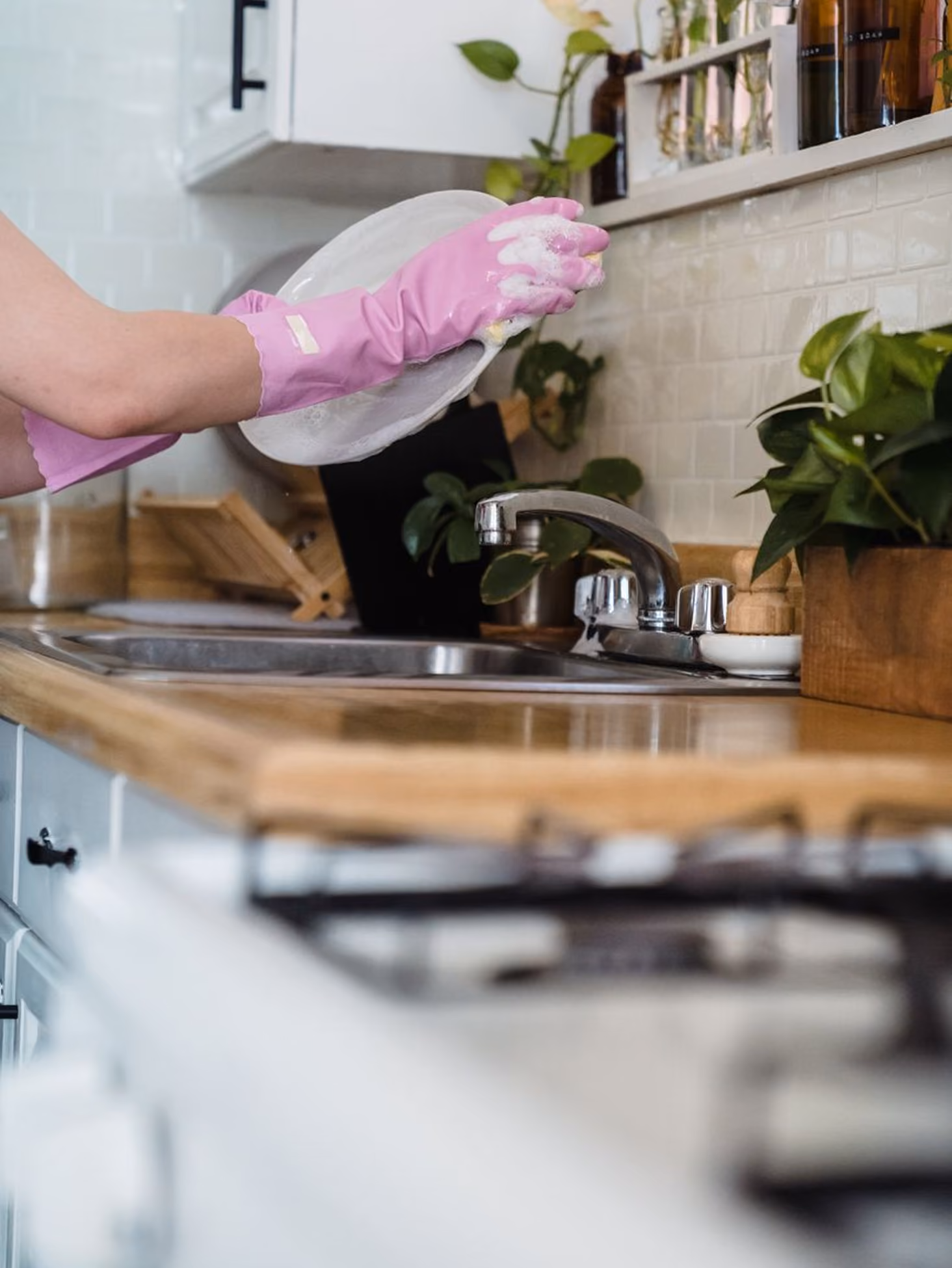 Person wearing pink gloves washing a white dish with soap suds over a kitchen sink.
