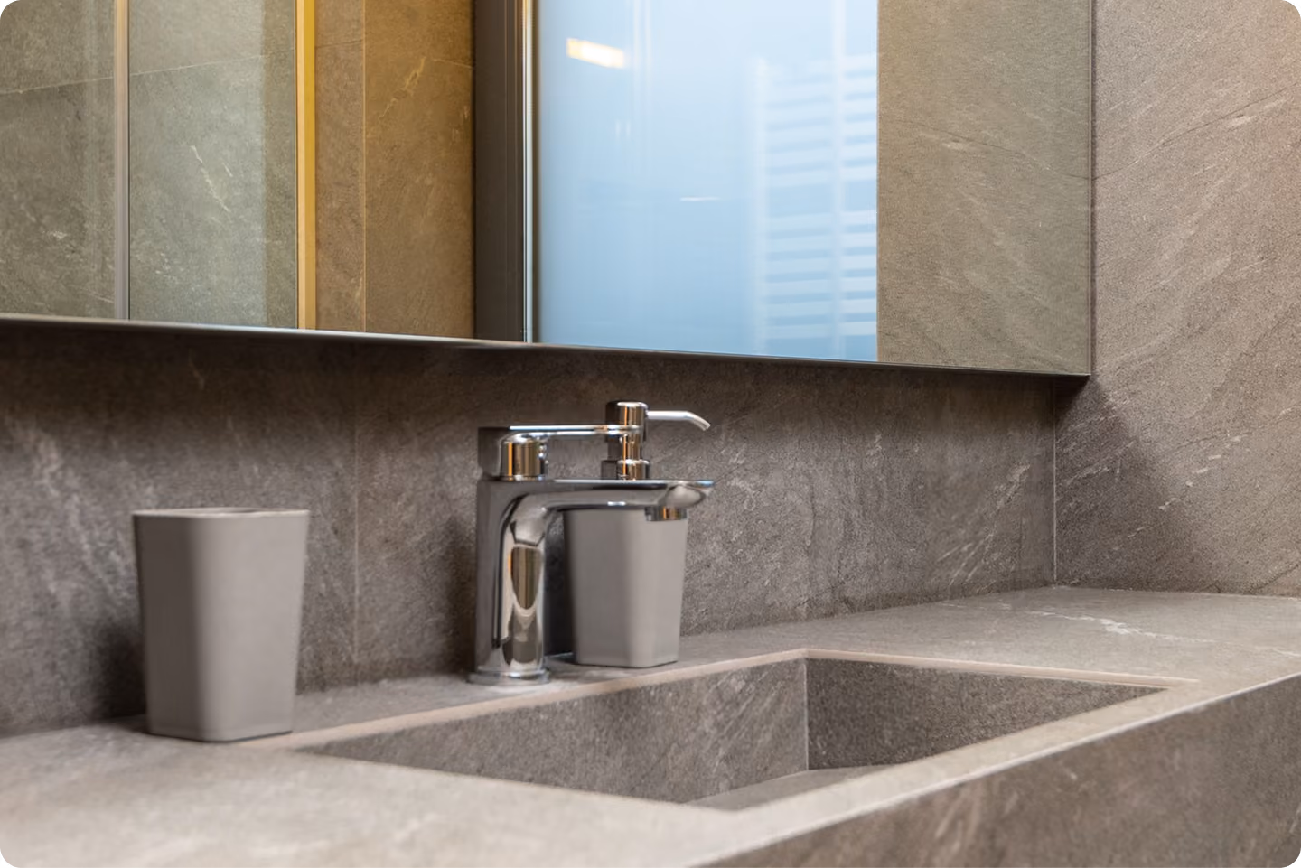 Modern gray stone bathroom sink with chrome faucet and two matching containers on the countertop.