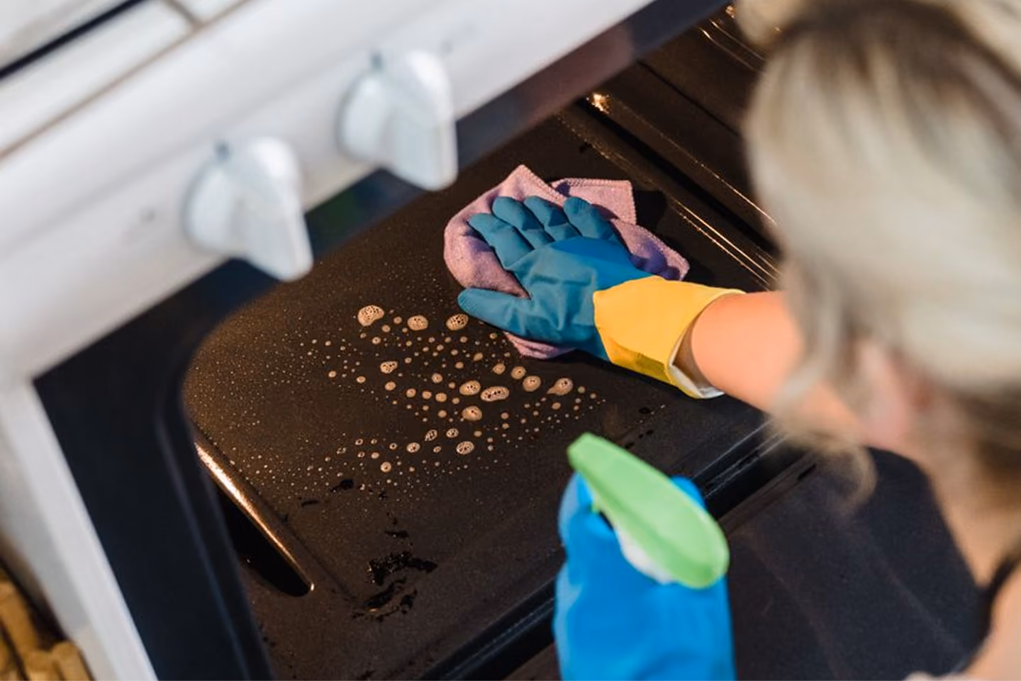Person wearing gloves cleaning the inside of an oven with a spray bottle and cloth.