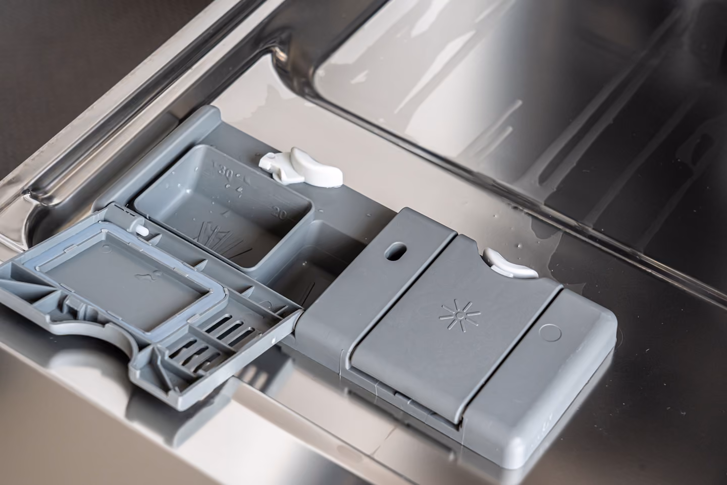 Opened dishwasher detergent dispenser with compartments for detergent and rinse aid.