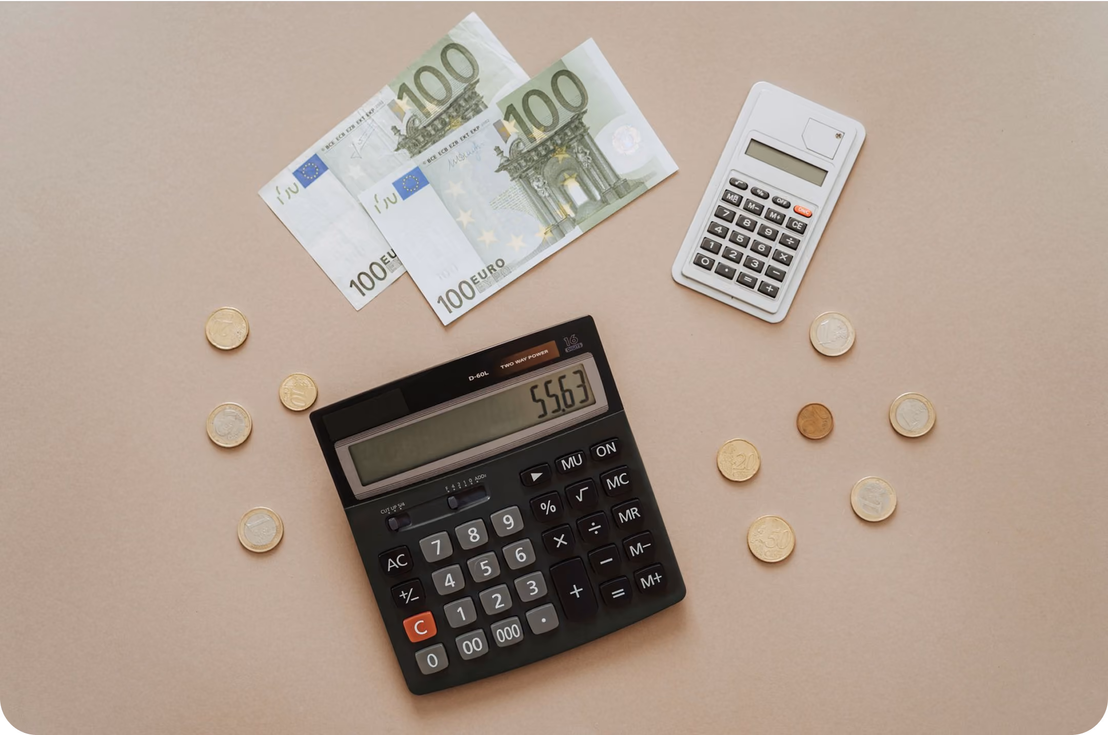 Two calculators surrounded by euro banknotes and assorted euro coins on a beige surface.