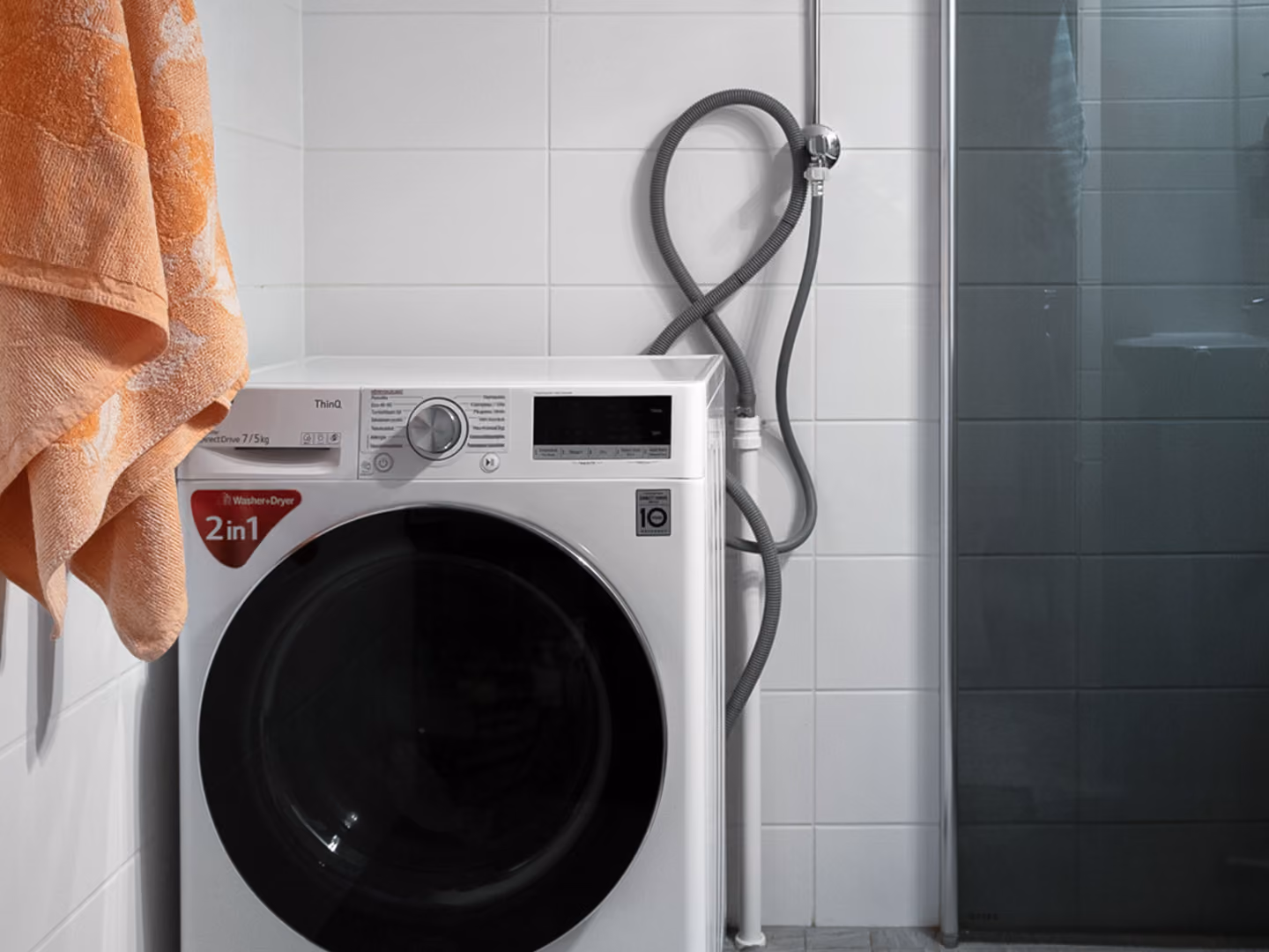 White front-load 2-in-1 washer dryer machine with orange towels hanging on the side.