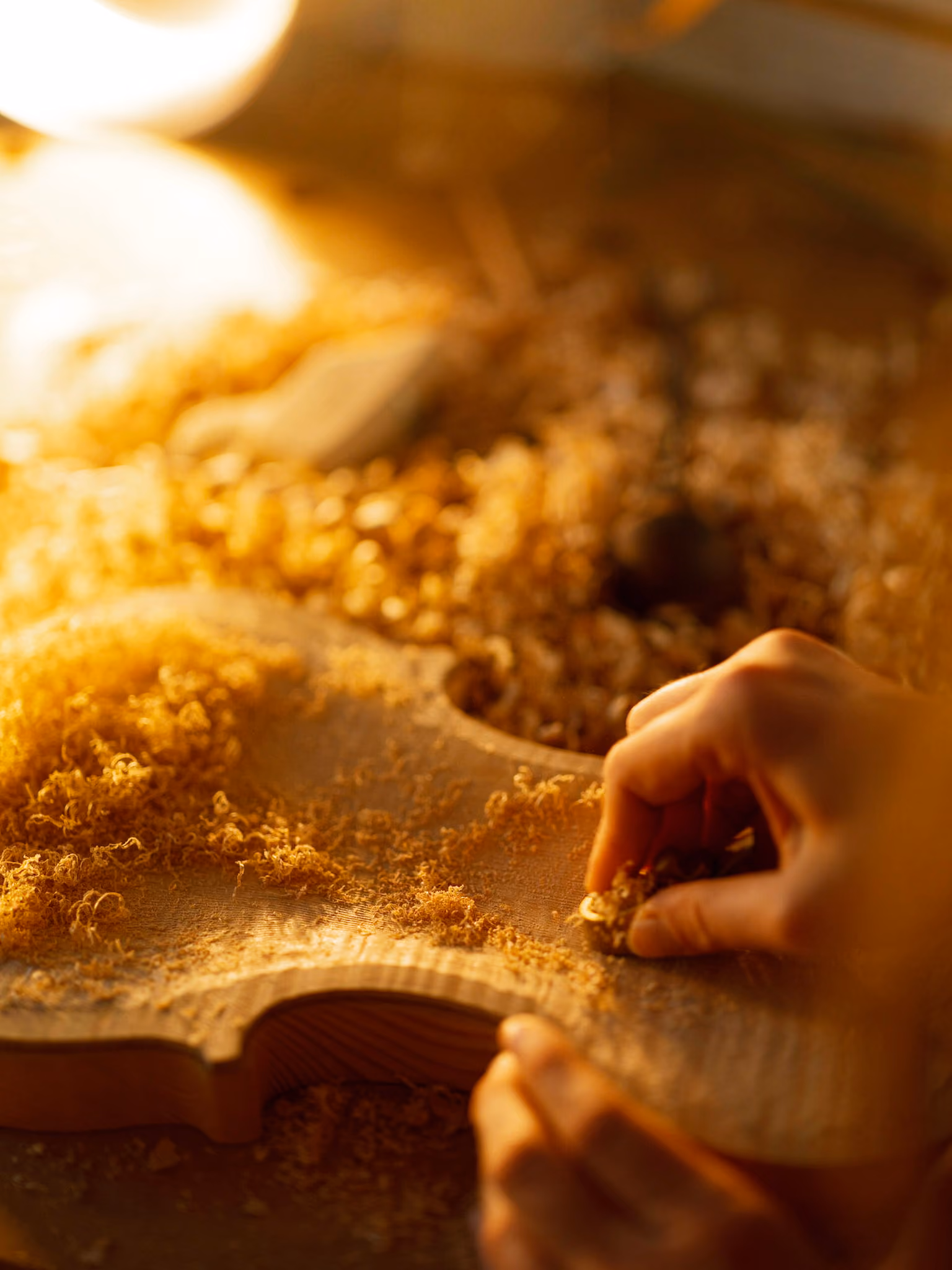 Hand sanding a wooden violin body surrounded by wood shavings in warm light.