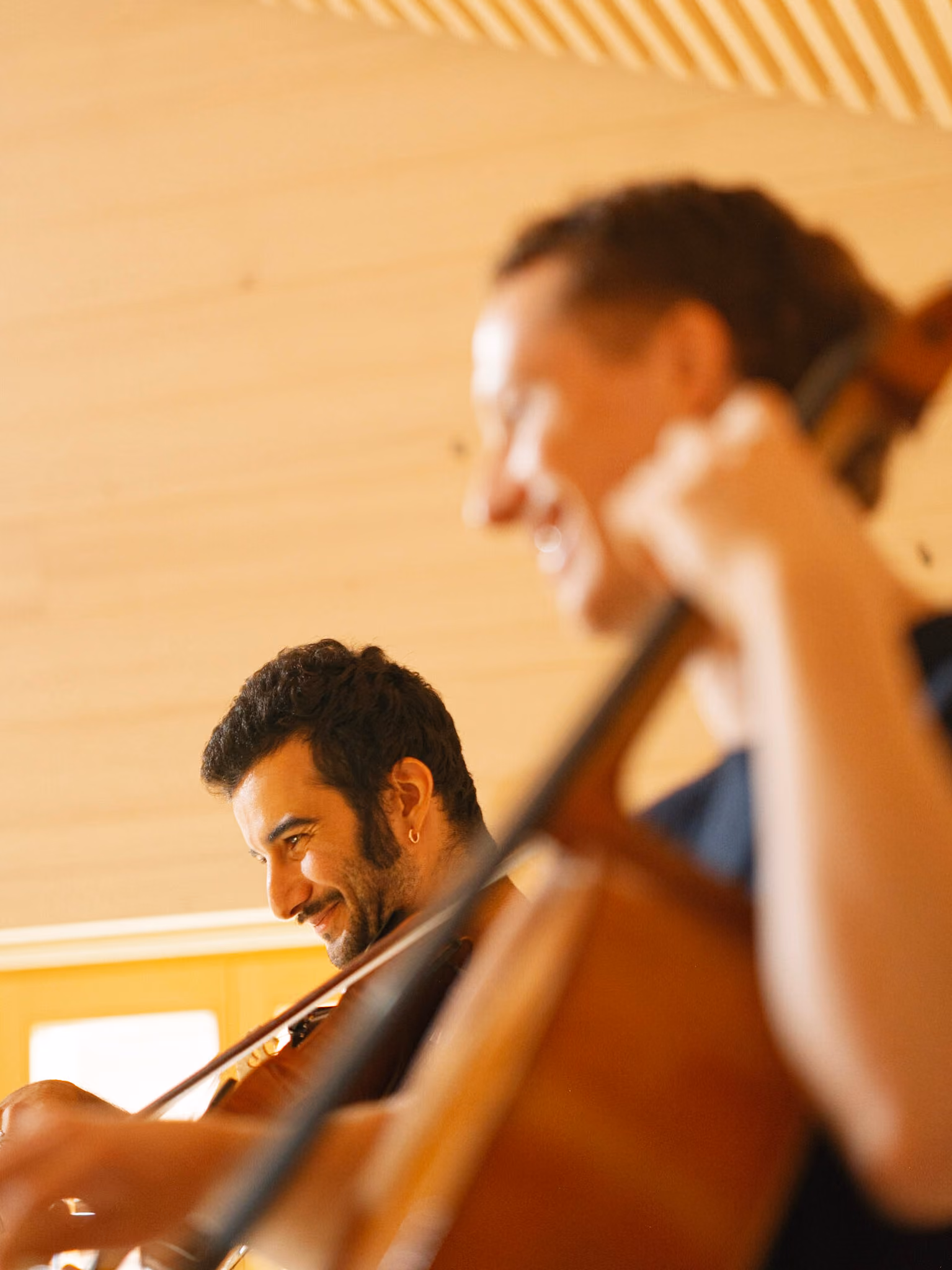 Zwei Musiker spielen Streichinstrumente in einem hellen Raum mit Holzwänden.