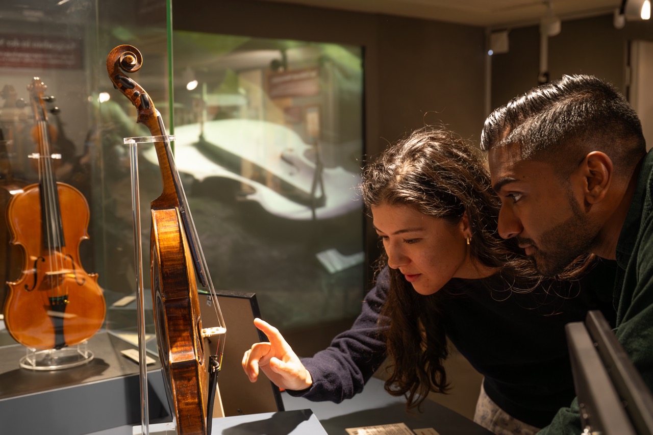 Zwei Personen betrachten ein antikes Streichinstrument hinter Glas in einem Museum.