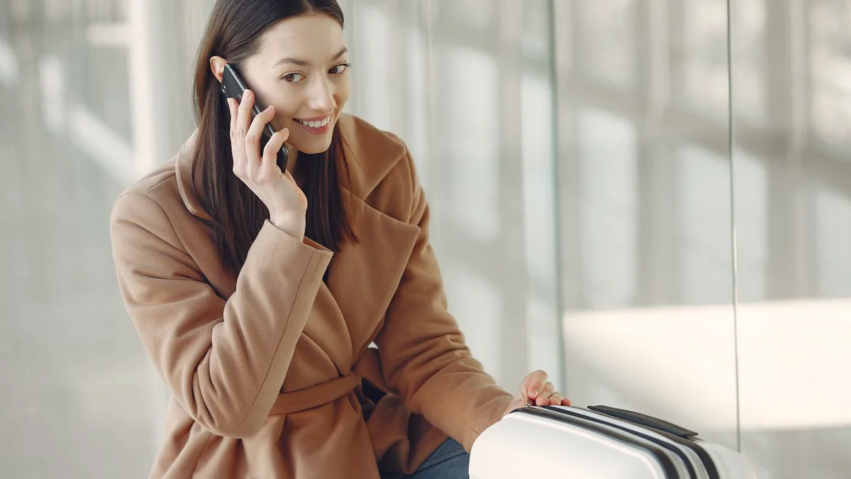 Traveller checking a phone beside a suitcase in an airport terminal