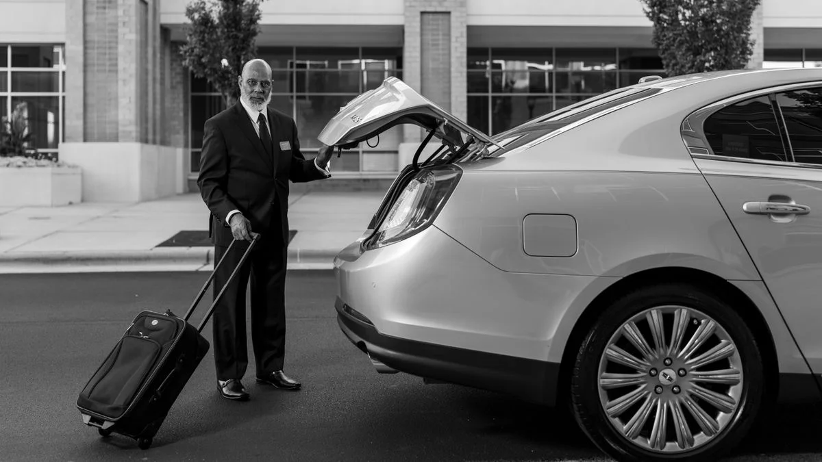 Chauffeur standing beside a car with passenger luggage