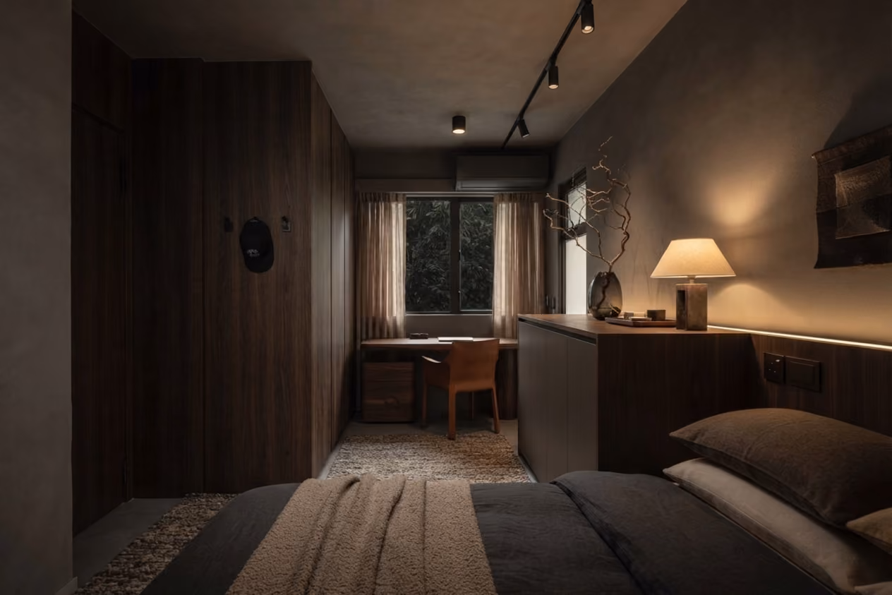 Cozy bedroom with dark bedding, wooden furniture, a desk by the window, and warm ambient lighting.
