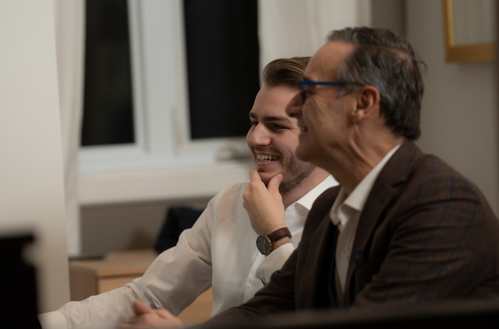 Deux hommes souriant et discutant ensemble dans un bureau, vêtus de vêtements professionnels.