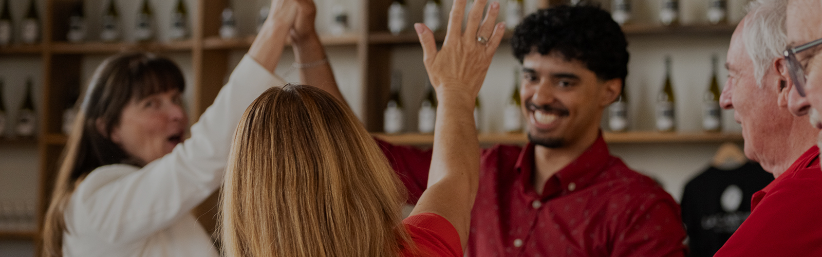 Quatre personnes souriantes se donnent un high five dans un lieu avec des bouteilles en arrière-plan.