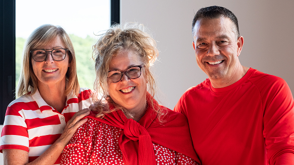 Trois personnes souriantes, dont deux femmes avec des lunettes et un homme en t-shirt rouge, posant ensemble.