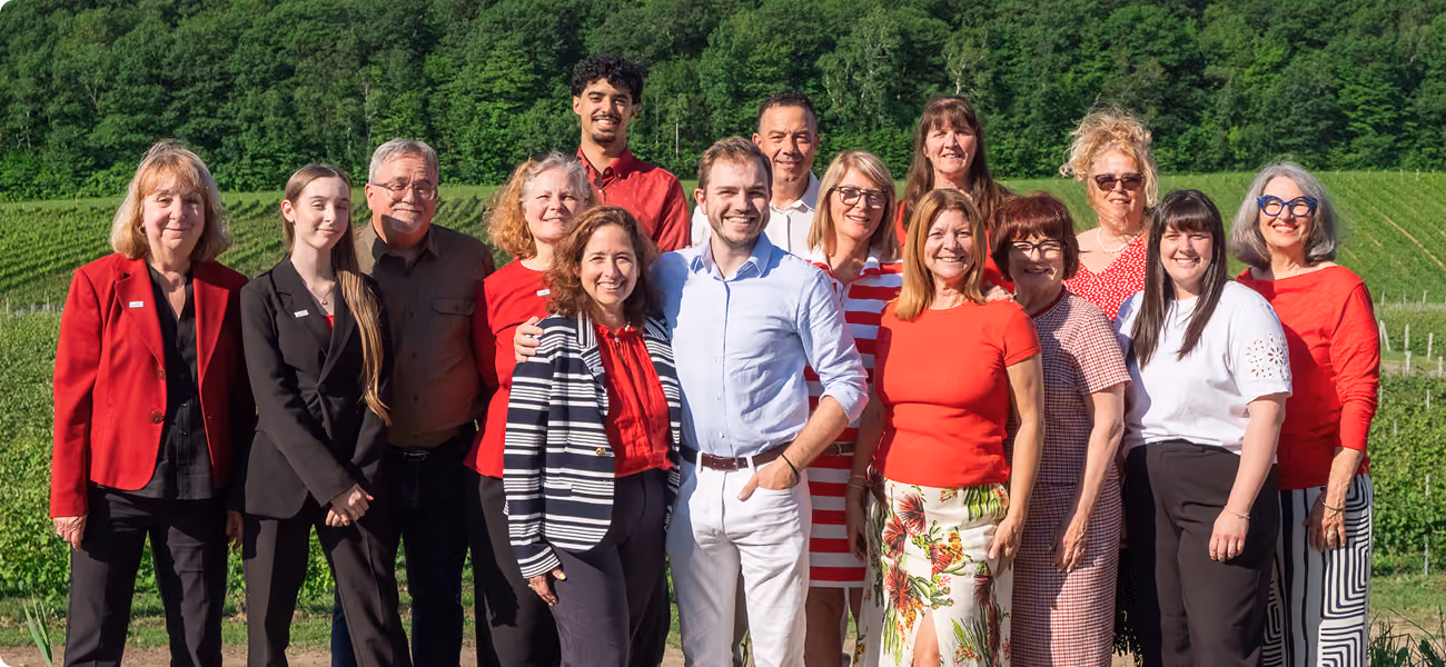 Groupe de 14 personnes souriantes posant à l'extérieur devant des vignes vertes sous le soleil.