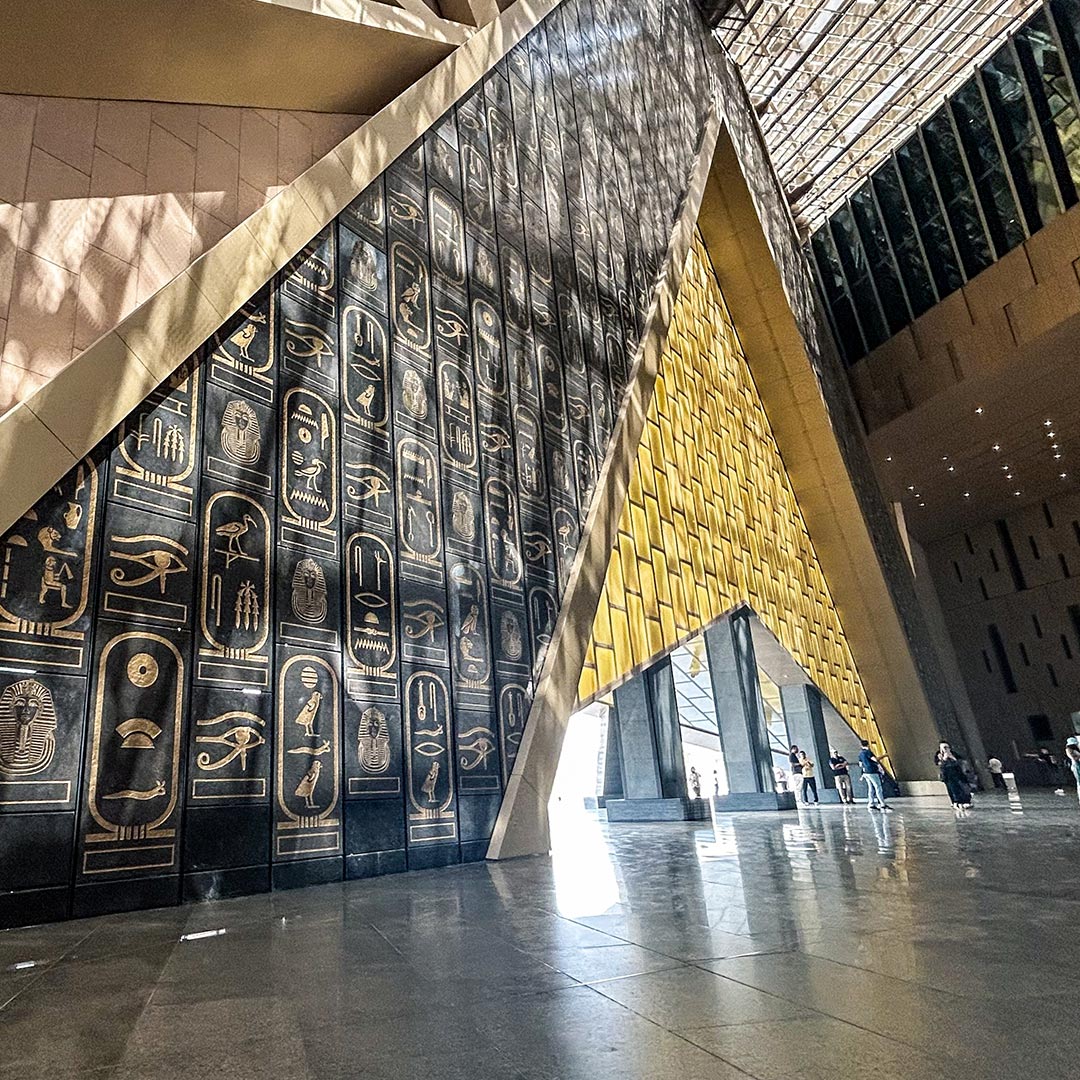 Interior of a large building with walls decorated in golden hieroglyphs and a patterned yellow wall.