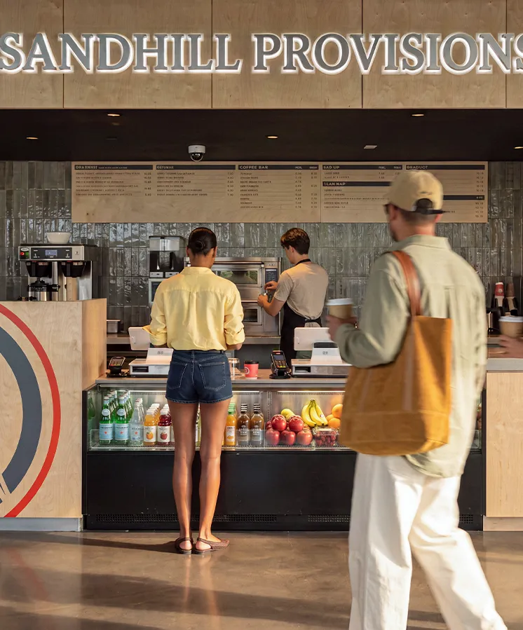 Customers order at Sandhill Provisions café counter with fruit and drinks on display.