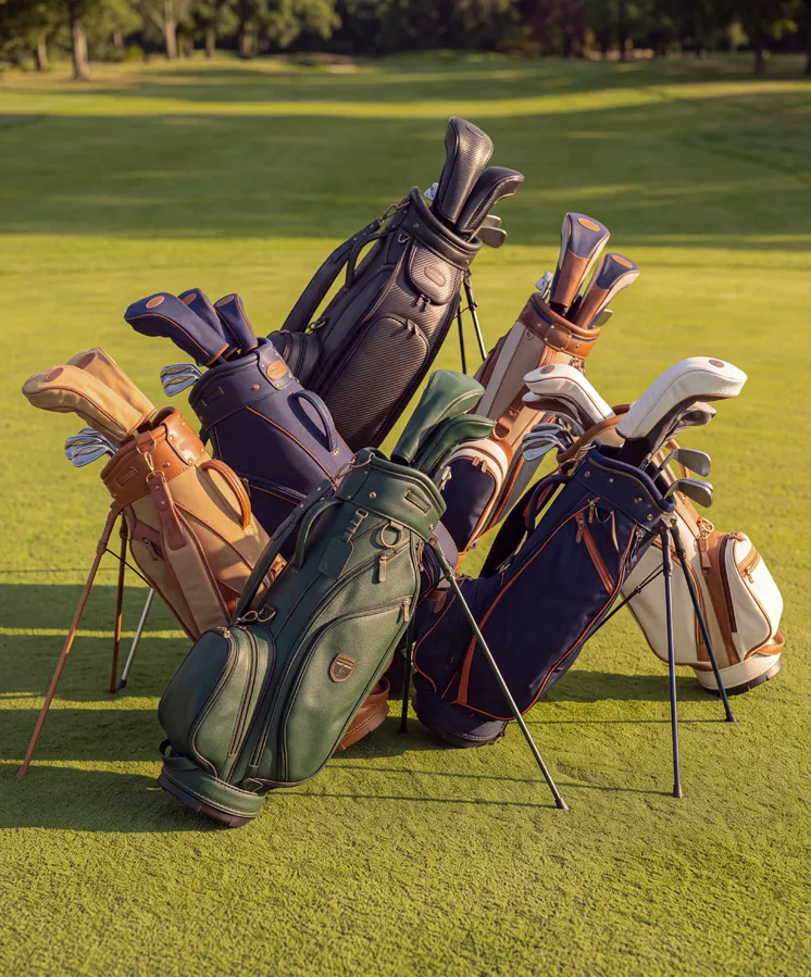 Group of golf bags with clubs standing on green golf course grass in sunlight.