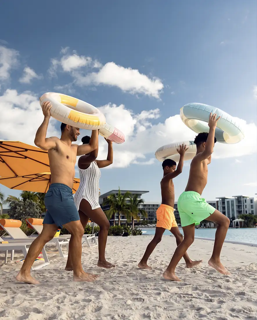 Family of four walking on a sandy beach holding inflatable pool rings over their heads.