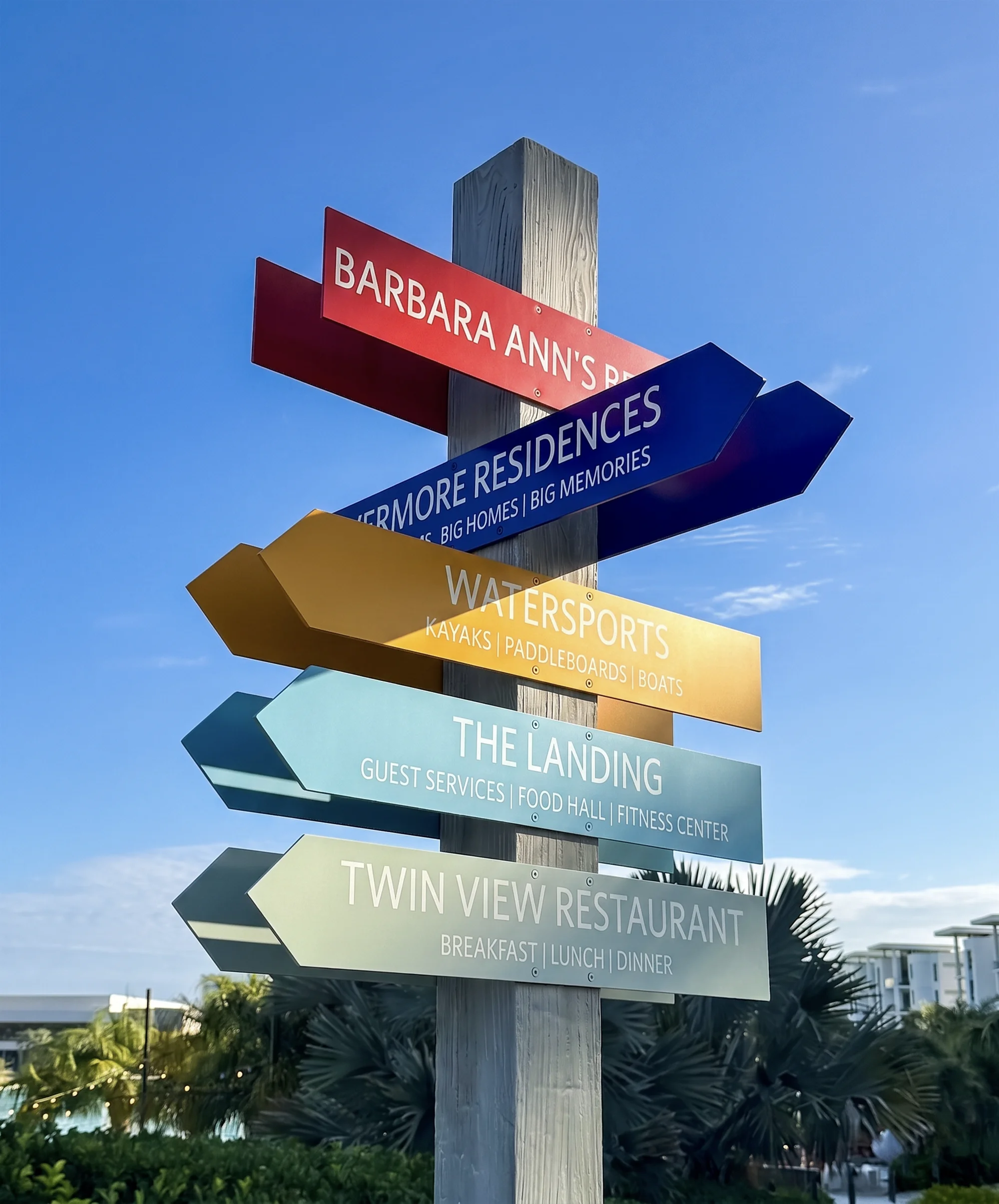 Colorful signage post with arrows pointing to restaurant, residences, watersports, guest services, and a restaurant.