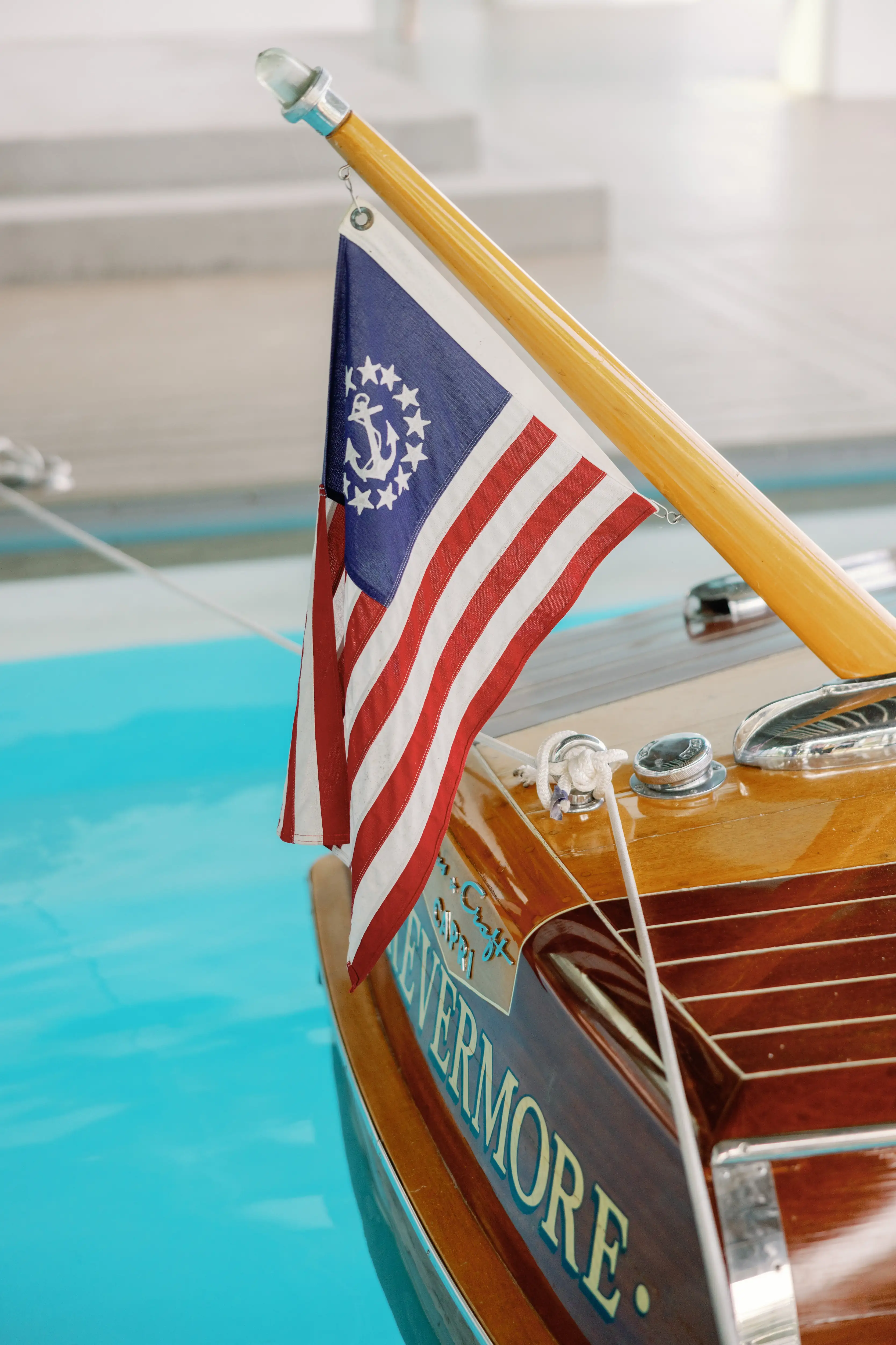 Rear view of wooden boat named Evermore with a blue and red nautical flag by a pool.