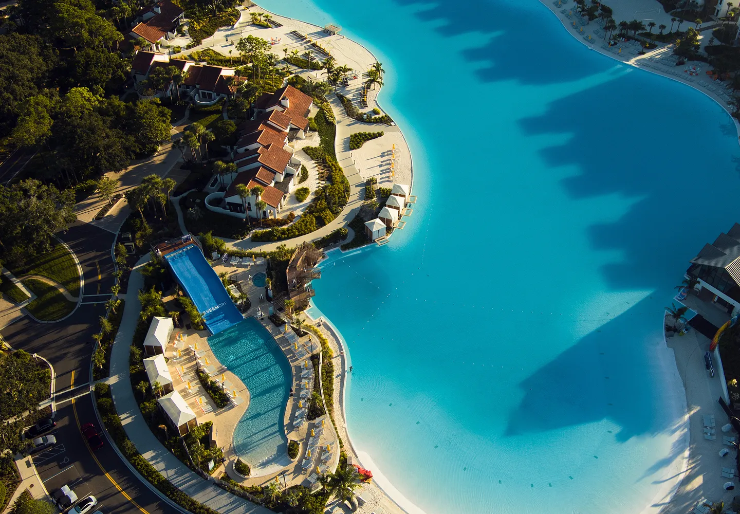Aerial view of a resort with a large blue lagoon-style pool, cabanas, and a water slide.