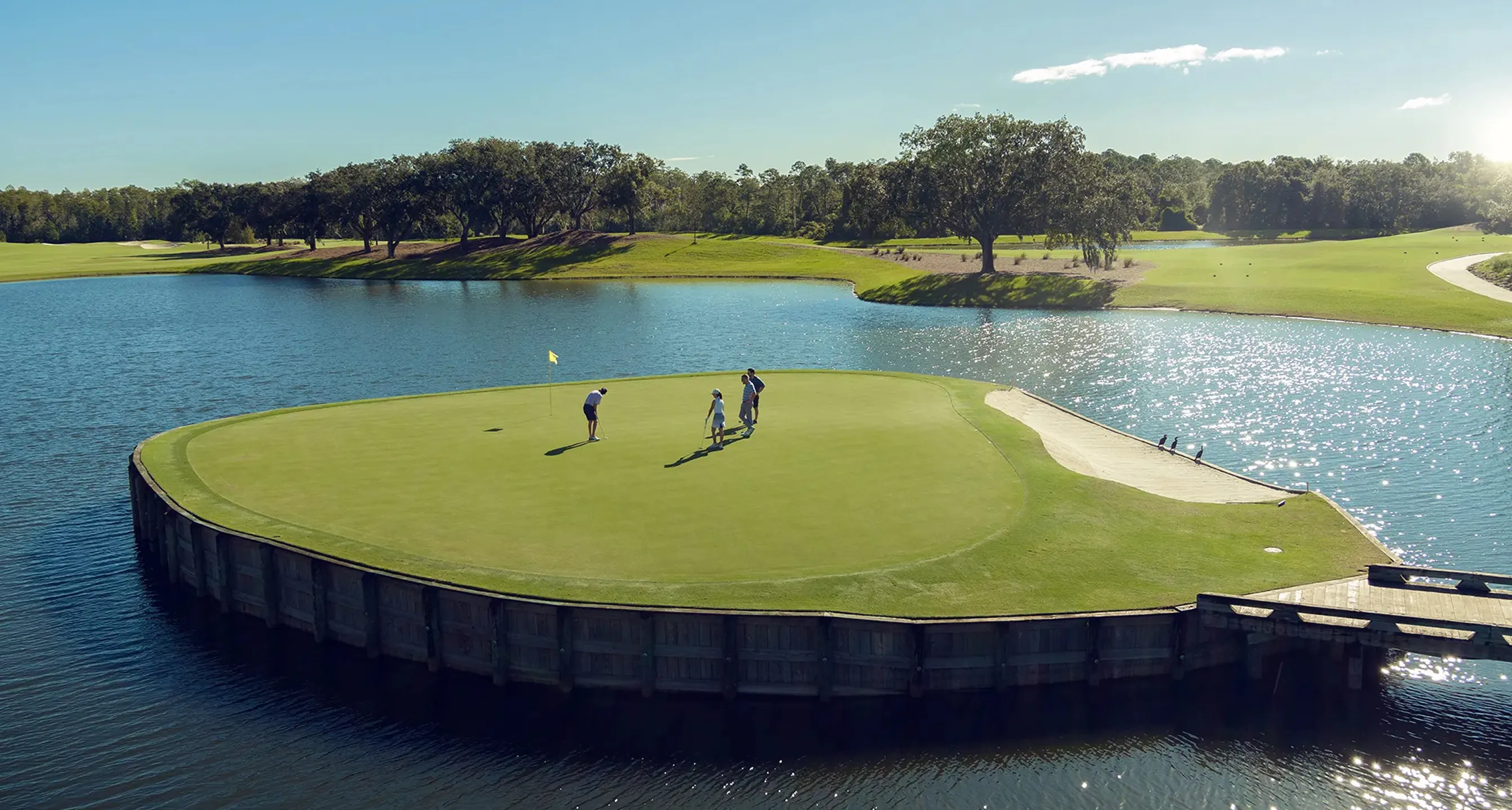 Three golfers on a green surrounded by water at a golf course during sunny day.