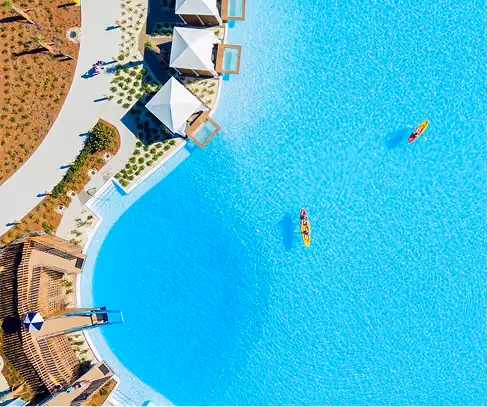 Aerial view of a large blue pool with two kayaks and poolside cabanas with people nearby.