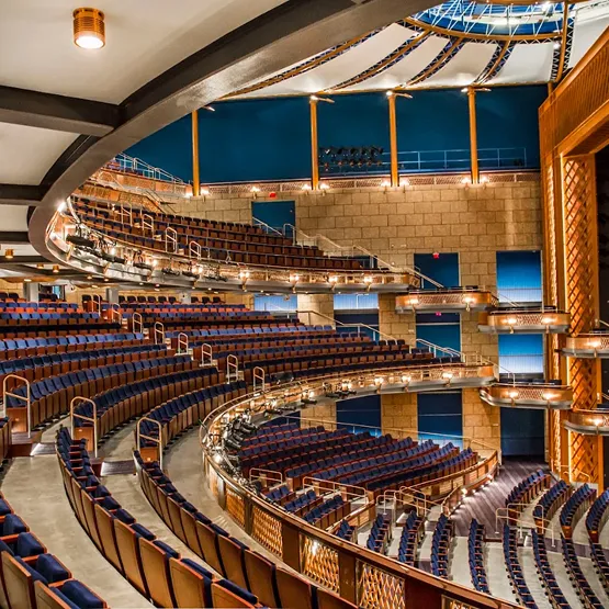 Curved balconies with rows of empty blue theater seats in a large, modern auditorium.