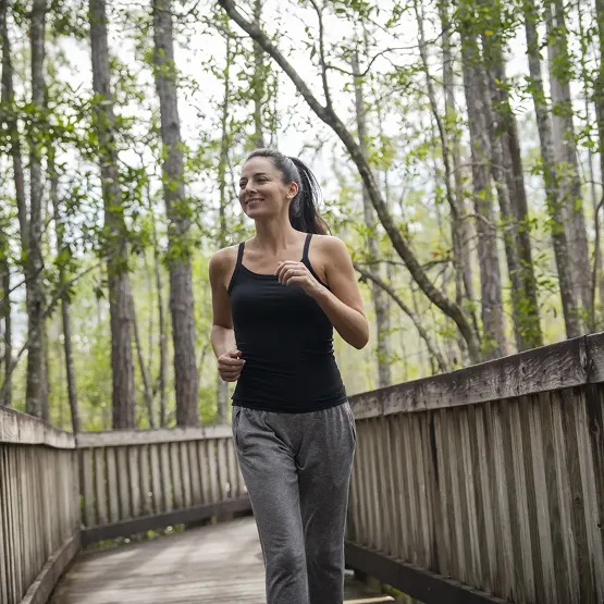 Woman jogging on a wooden path in a forest with trees surrounding her.