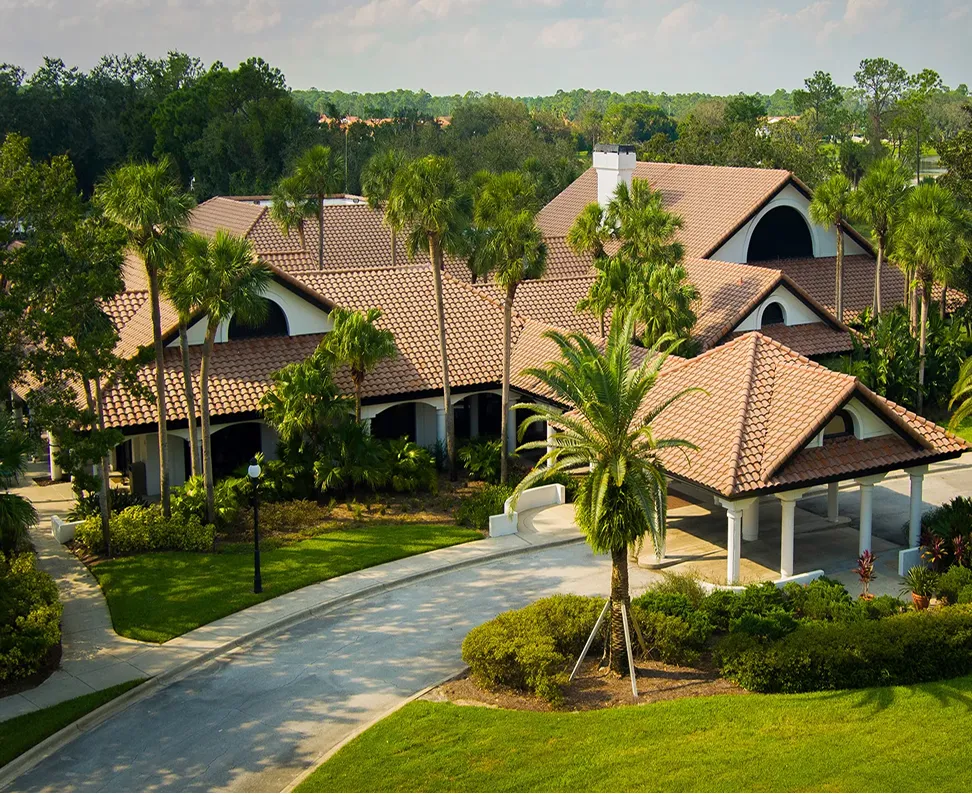 Spanish-style building with terracotta roof surrounded by palm trees and green landscaping.