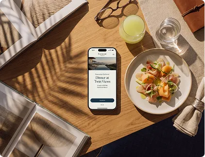 Mobile phone on wood table showing restaurant app next to fresh salad, glasses, napkin, and open books.