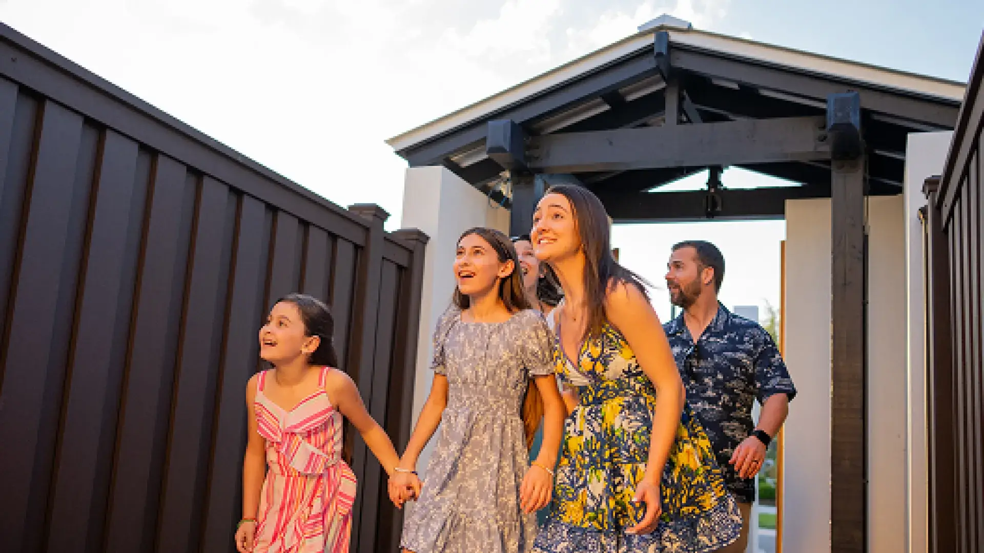 Four people walking outside near fences, looking up with excited expressions at sunset.