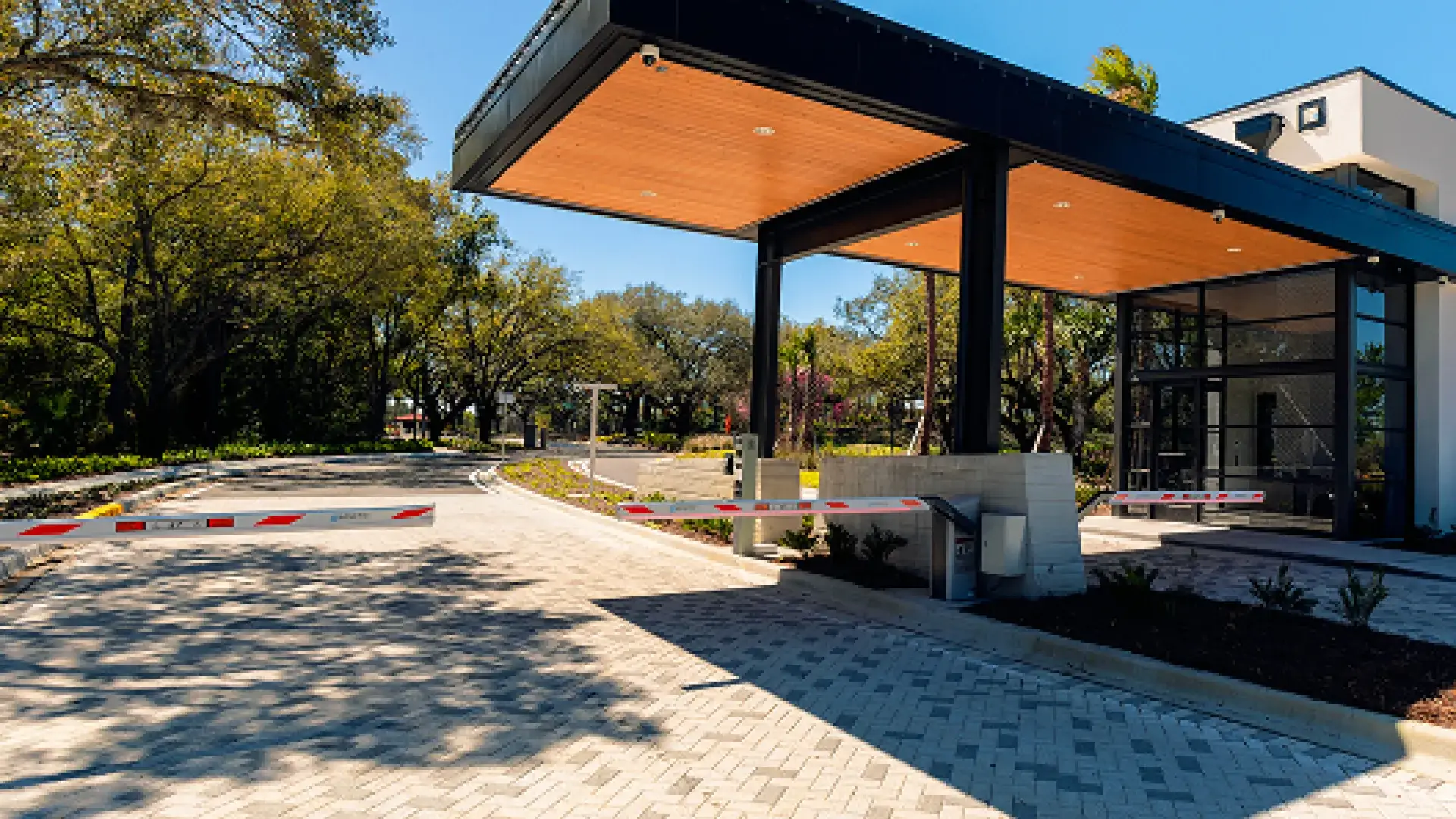 Modern secured driveway entrance with automatic barriers and a canopy with wooden ceiling panels.