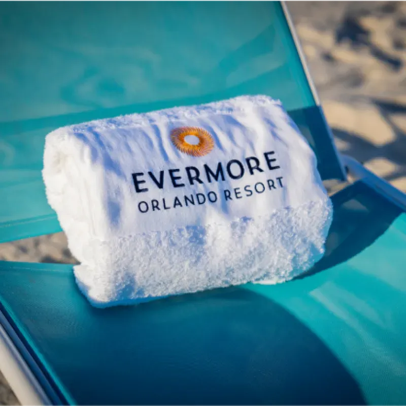 White towel embroidered with Evermore Orlando Resort logo on a teal lounge chair near sandy beach.