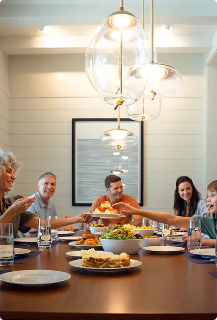 A family sharing food and smiling around a dining table with modern pendant lights overhead.