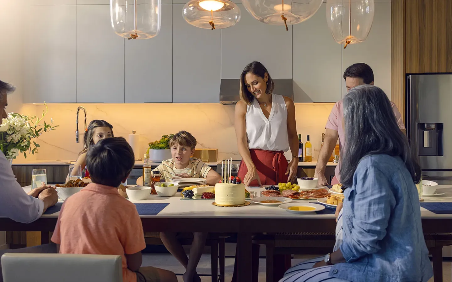 Family gathered around a kitchen island with food and a birthday cake with candles.