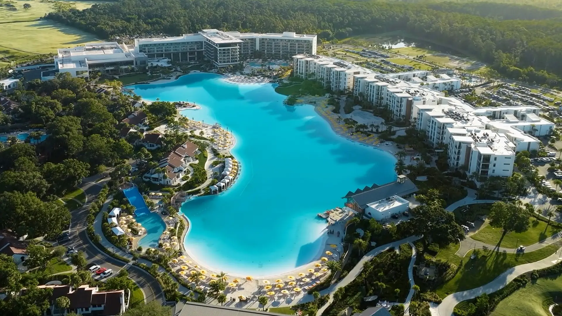 Aerial view of a large blue lagoon pool surrounded by resort buildings and lush greenery.