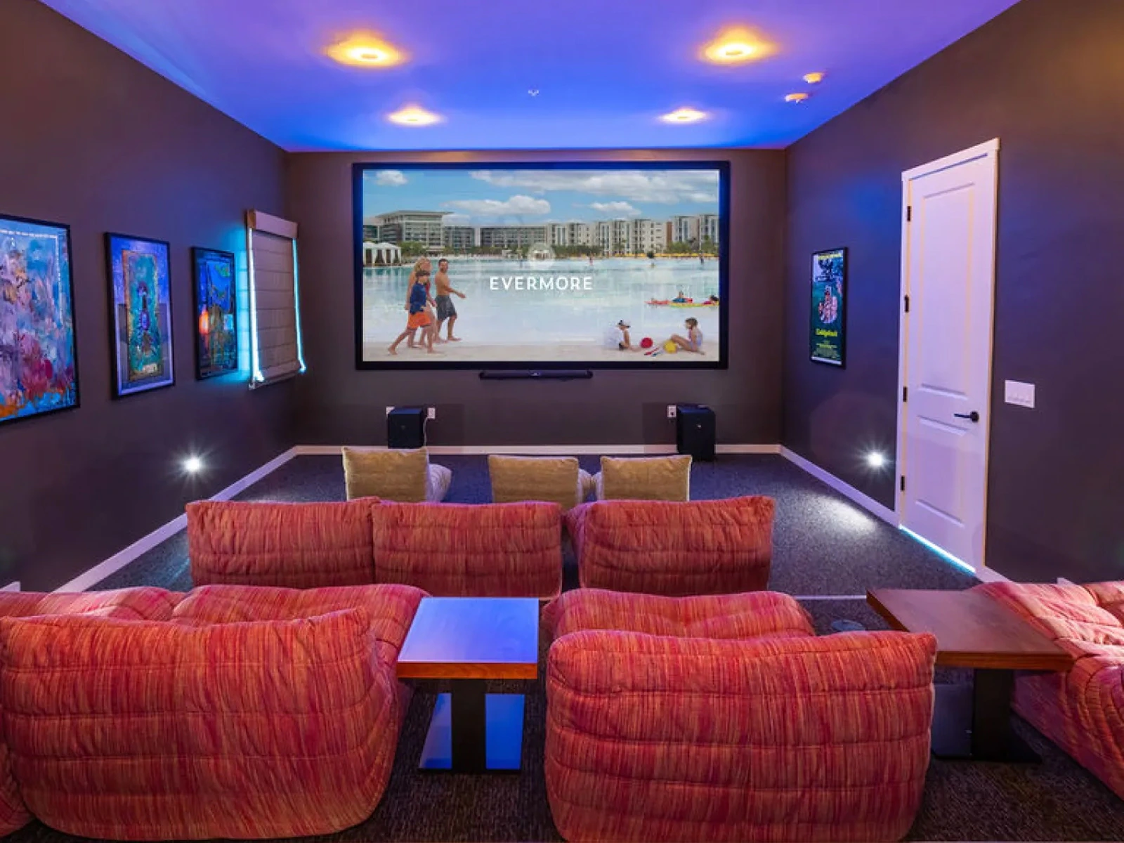 Home theater room with red cushioned seats, three smaller chairs, and a large screen showing 'EVERMORE'.