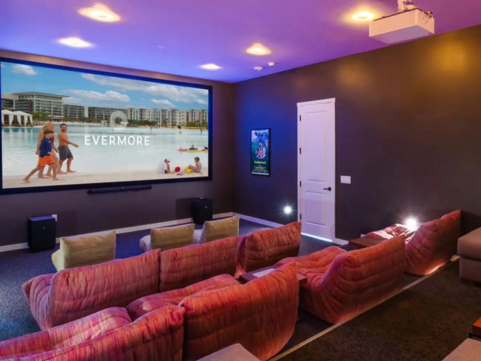 Home theater with tiered pink and beige seating facing a large screen displaying 'EVERMORE' beach scene.