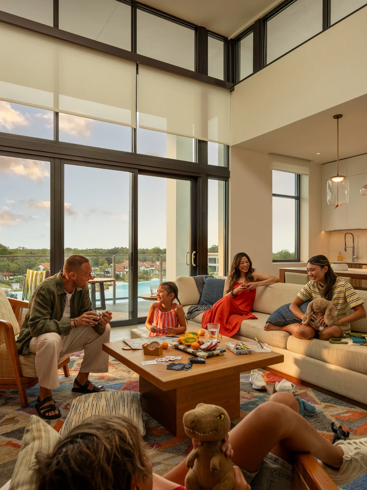 Family of four enjoying time in a bright living room with large windows and a coffee table with snacks.
