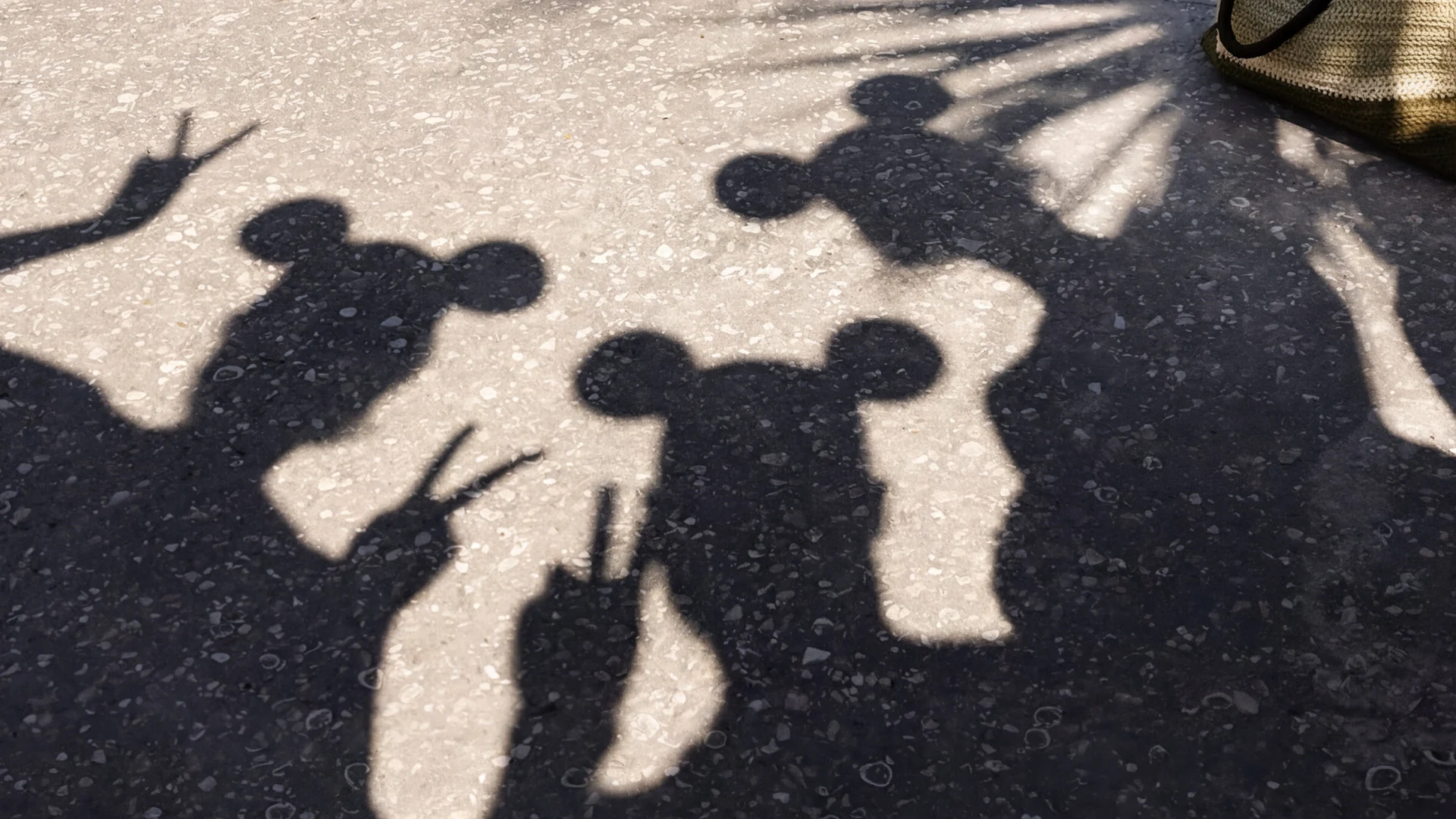 Shadows of three people with Mickey Mouse ear hats making peace signs on a textured surface.