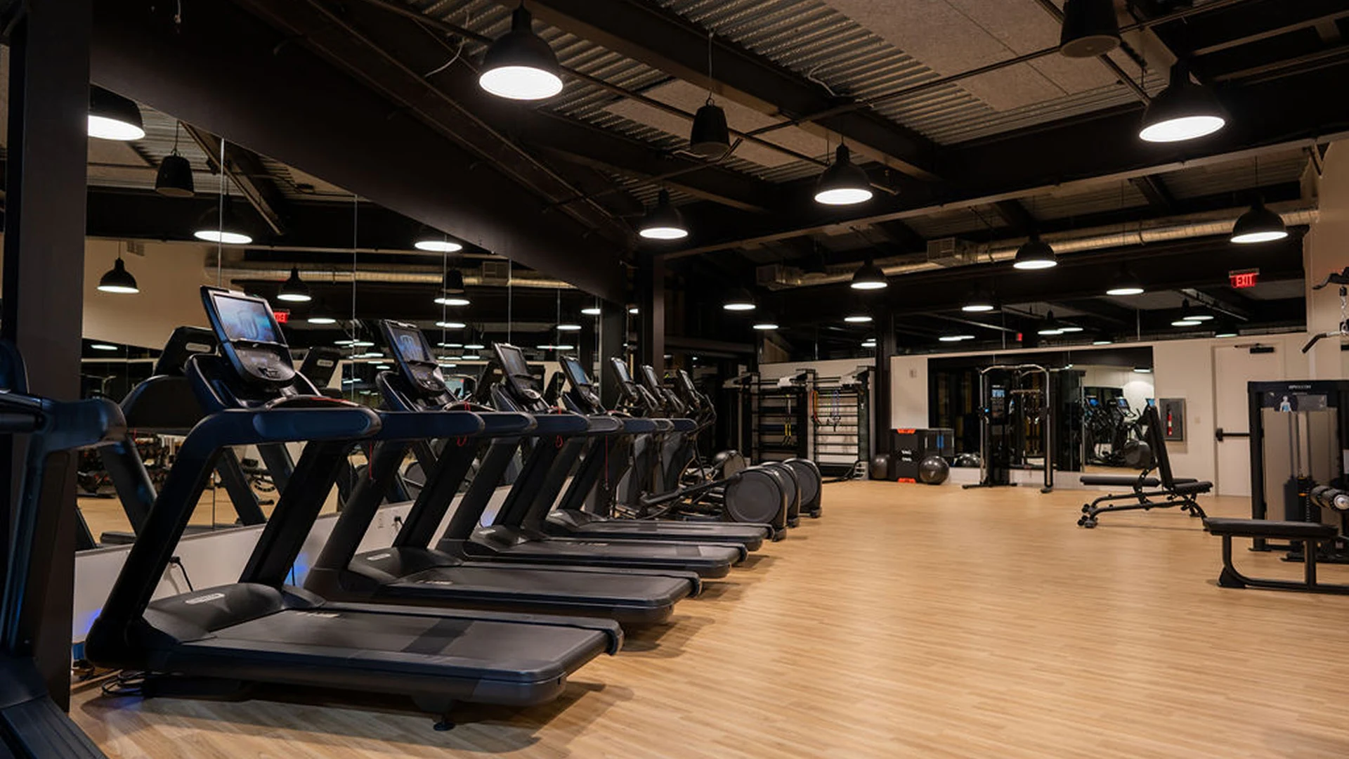 Row of treadmills lined up inside a modern gym with wooden floors and various workout machines.