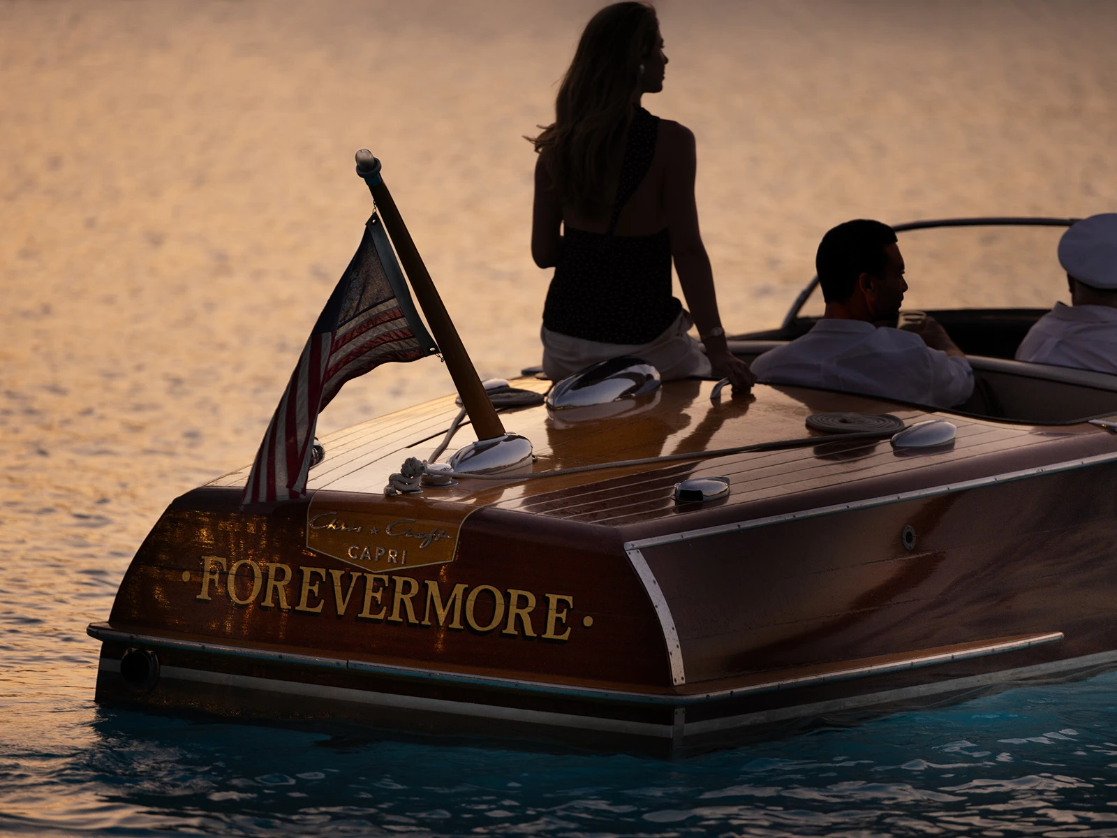 People on a wooden boat named Forevermore at sunset with an American flag at the stern.