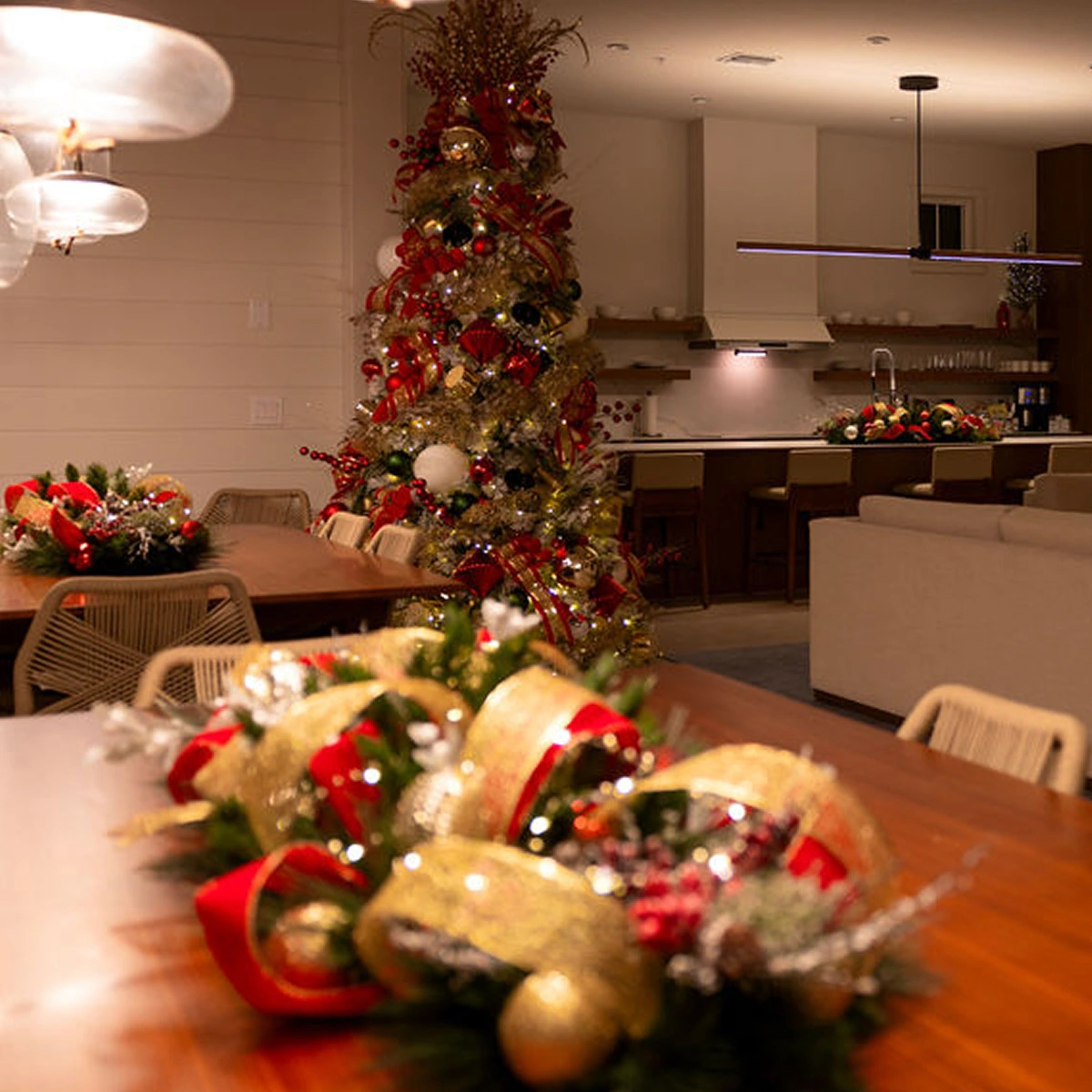 Dining and living area decorated for Christmas with a lit tree, wreaths, and festive red and gold accents.