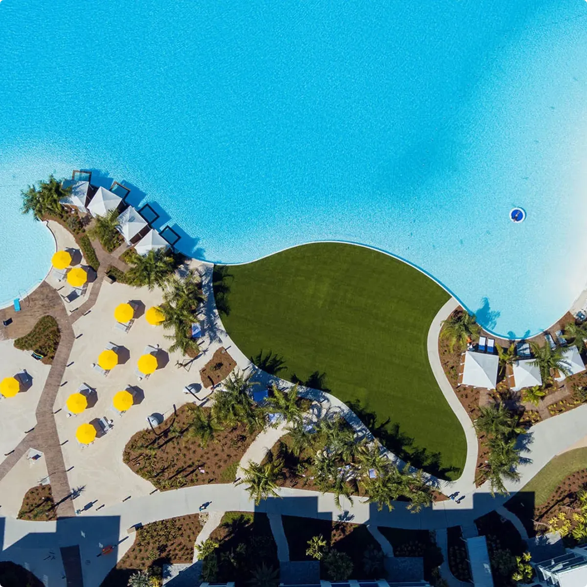 Aerial view of a large pool with yellow umbrellas, white cabanas, and green lawn area.