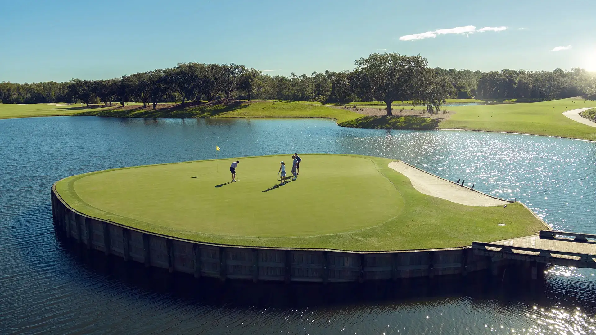 Three people playing golf on an island green surrounded by water on a sunny day.