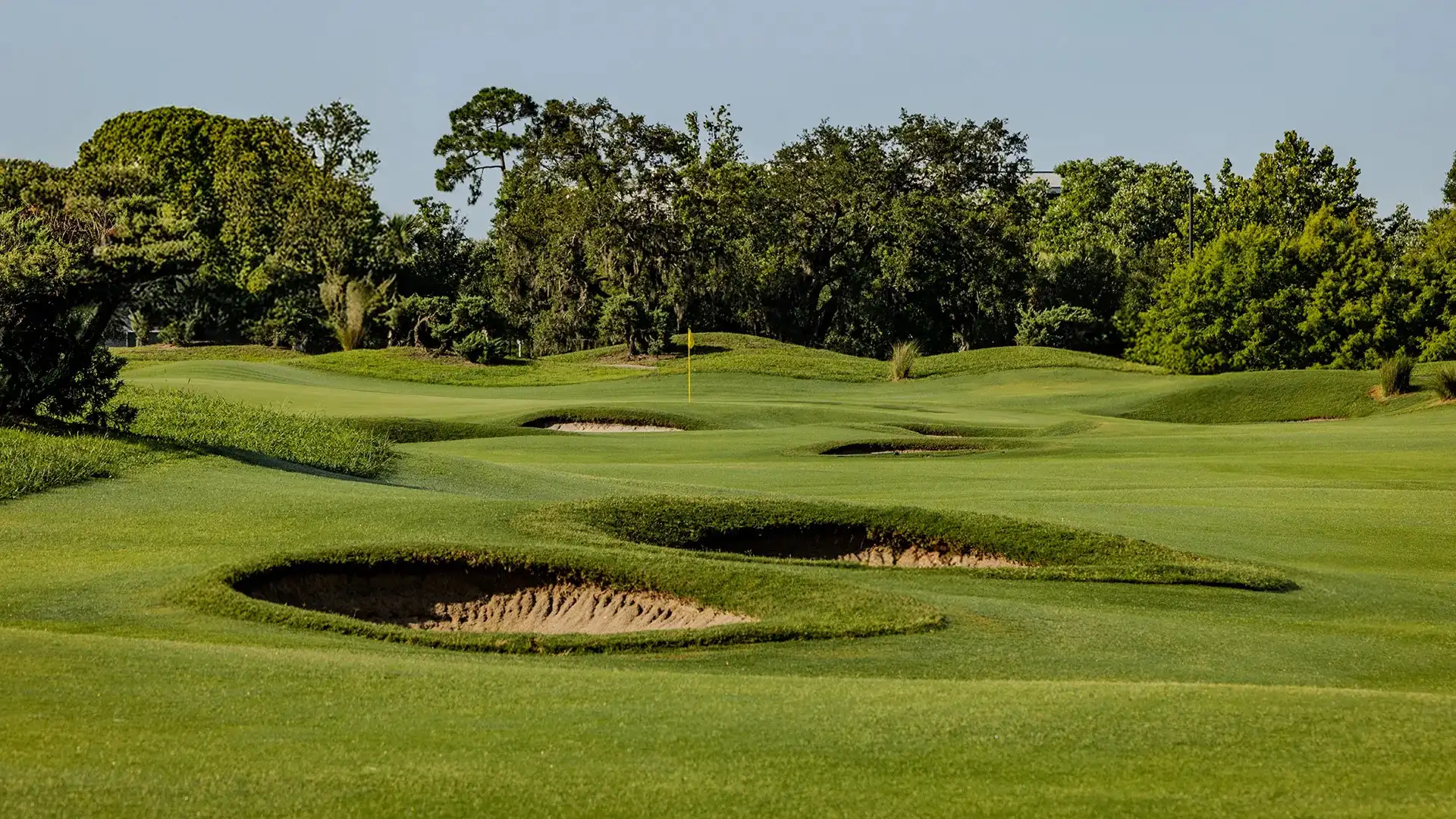 Golf course fairway with sand bunkers surrounded by trees and clear sky.