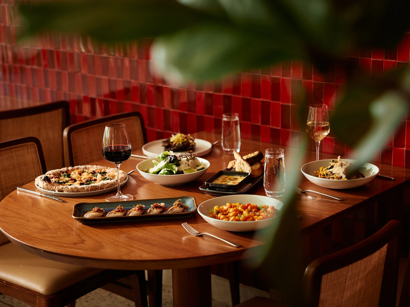 Wooden table set with pizza, salad, pasta, sushi, dip, bread, and glasses of red and white wine.