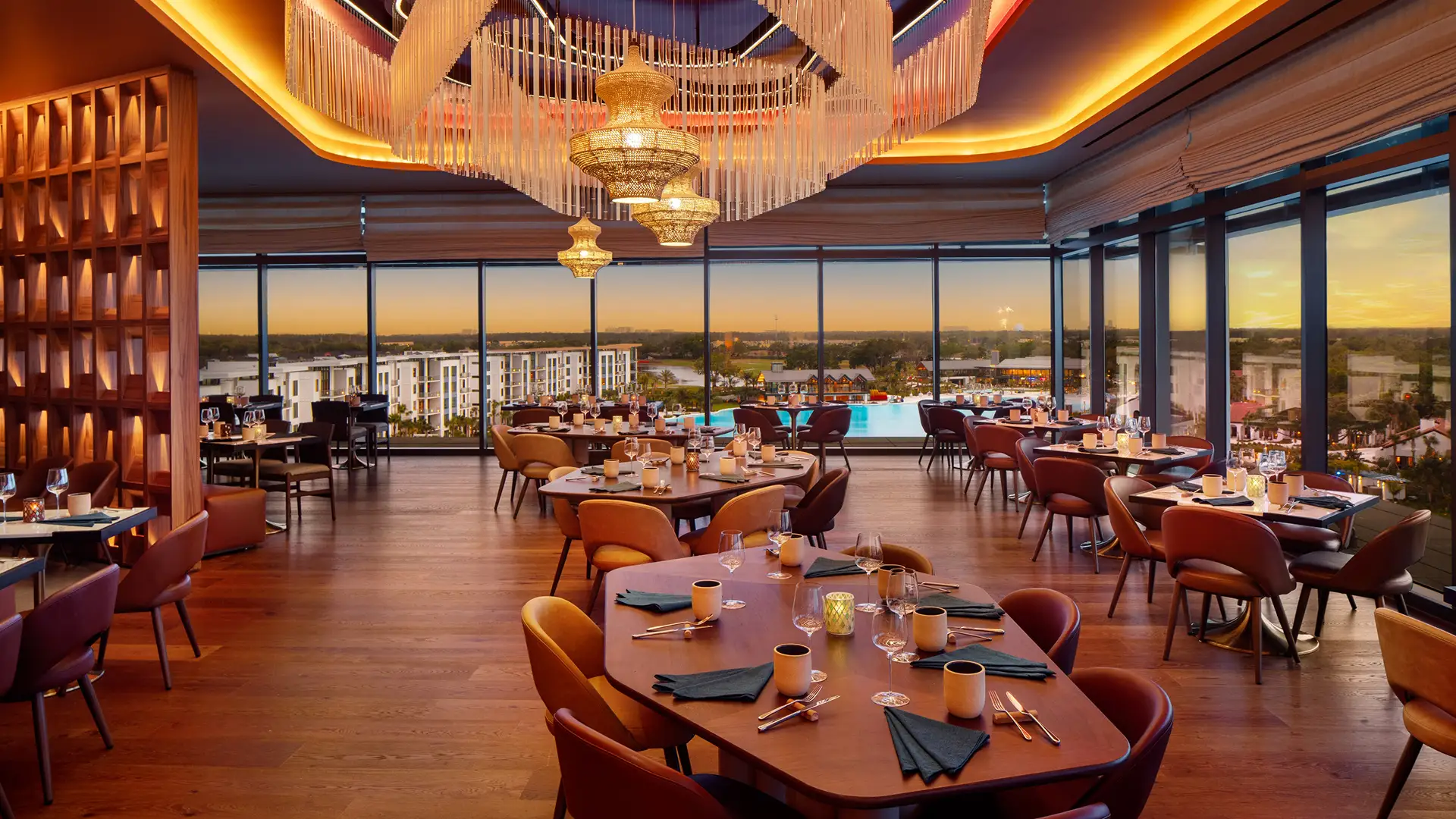 Upscale dining room with large windows overlooking a pool and distant buildings at sunset.