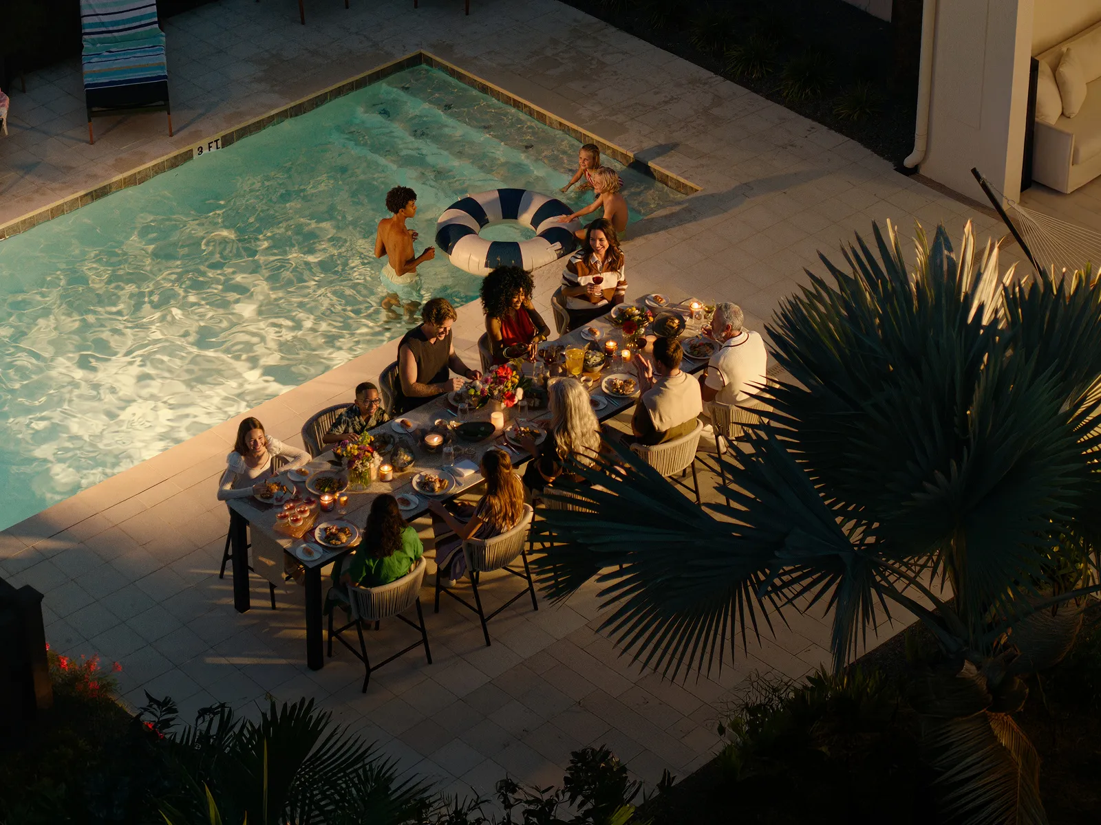 Group of people enjoying an evening meal at a poolside table with candles and food.