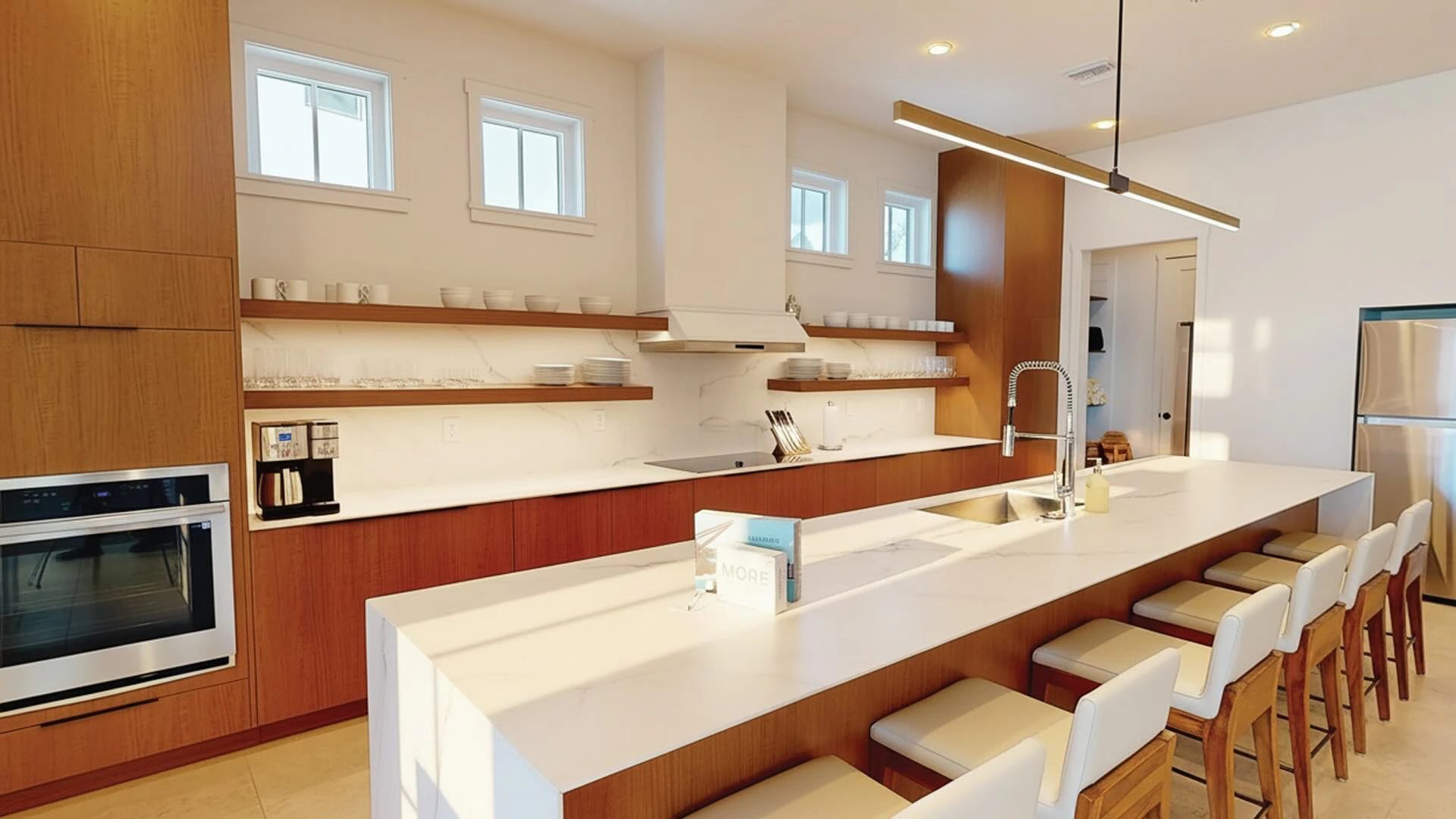 Modern kitchen with white island, wooden cabinets, six stools, stainless appliances, and open shelves.