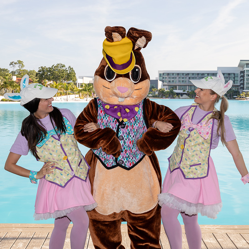 Two women in Easter bunny costumes posing with a large Easter bunny mascot by a pool.